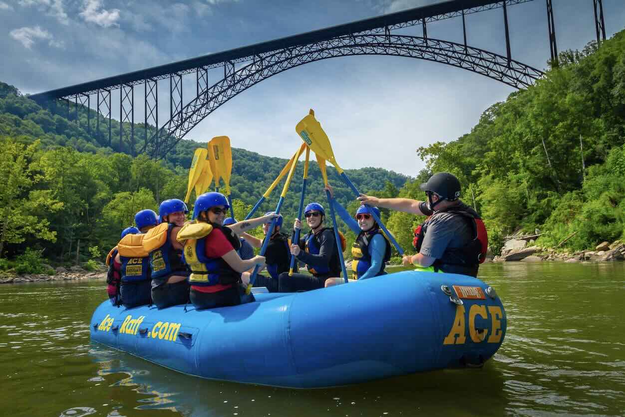 group of rafters below the new river gorge bridge giving a paddle high five